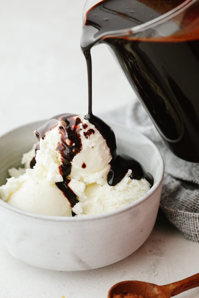 Chocolate sauce being poured onto some vanilla ice cream. 