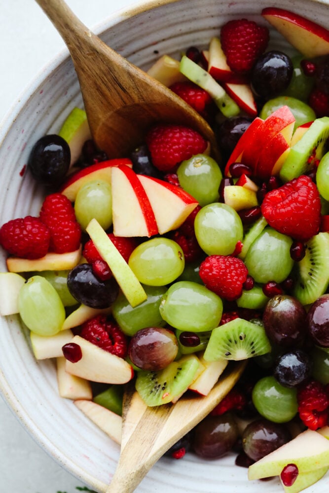 Christmas fruit salad in a bowl with a wooden spoon. 