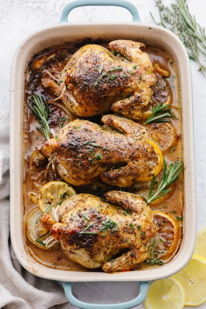 Cooked cornish hens in a baking dish with garnish. 