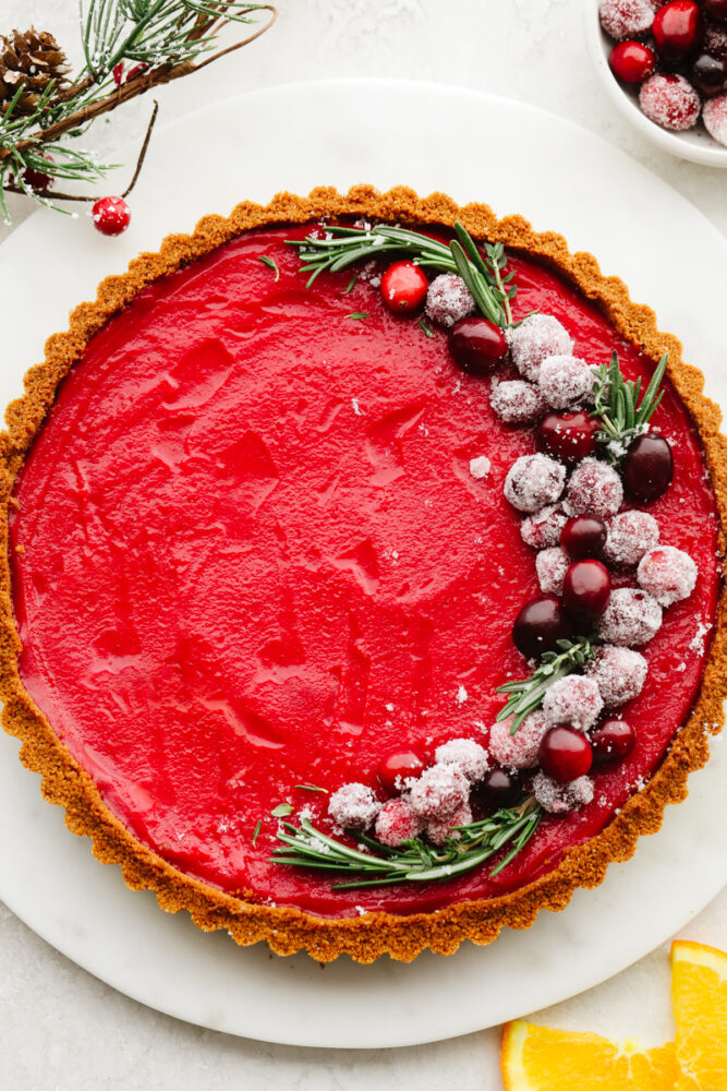 A full cranberry curd tart, topped with sugared cranberries and rosemary garnish.