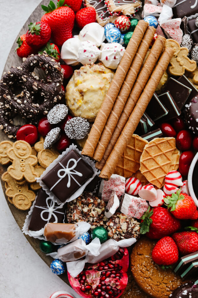 A zoomed in shot of some chocolates, cookies, fruit and candy on a wooden board. 