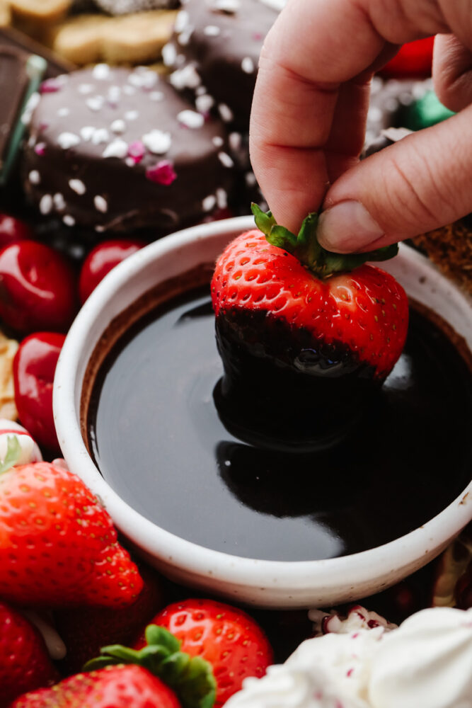 A strawberry being dipped into chocolate sauce. 