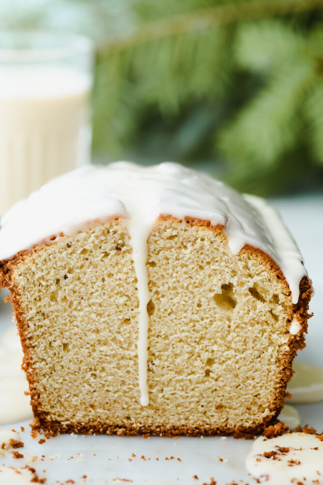 A side view of a loaf of eggnog quick bread with an eggnog glaze dripping down. 