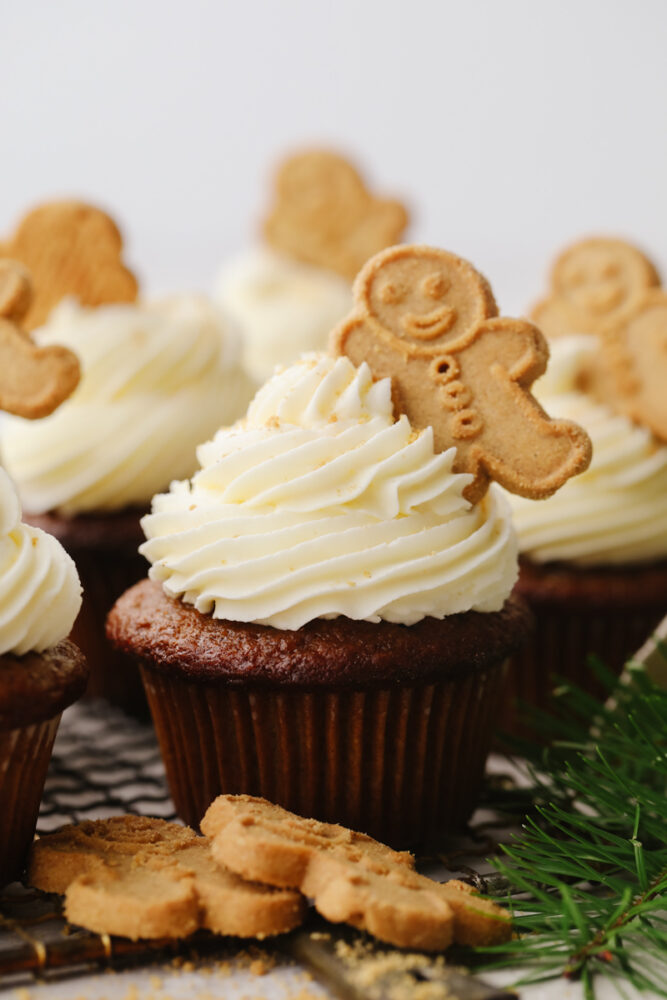 A gingerbread cupcake with frosting and a gingerbread cookie on top.