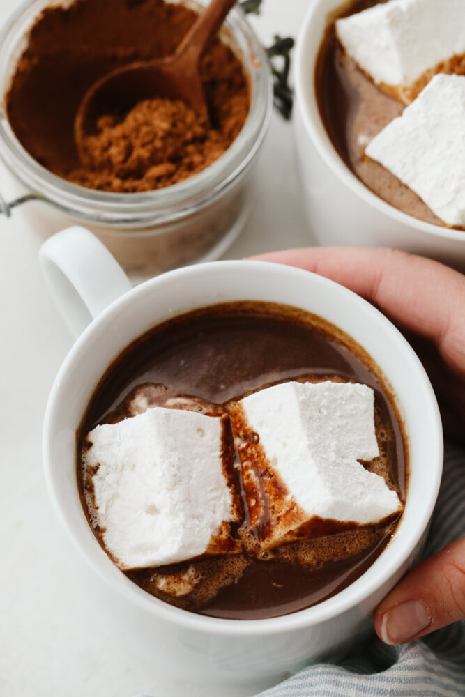 Holding a white mug filled with hot chocolate and marshmallows.