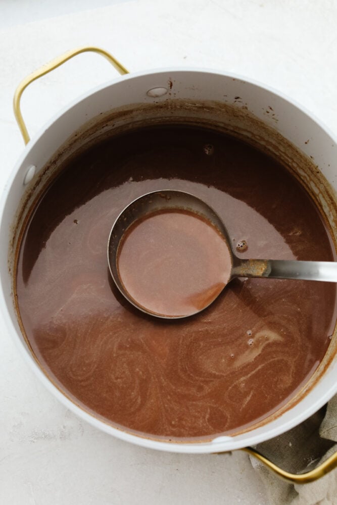 Hot chocolate in a large pot being scooped up with a ladle.