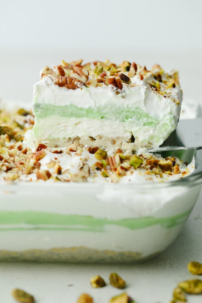 A slice of pistachio dessert being taken out of a 9x13 baking pan. 