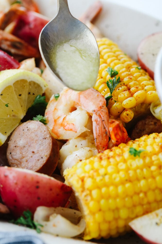 A southern classic, this shrimp boil recipe includes corn, potatoes, sausage, and shrimp boiled together in one pot and packed full of delicious flavor! It's a tried and true favorite that you don't want to miss! Melted butter being drizzled onto ingredients from a spoon.