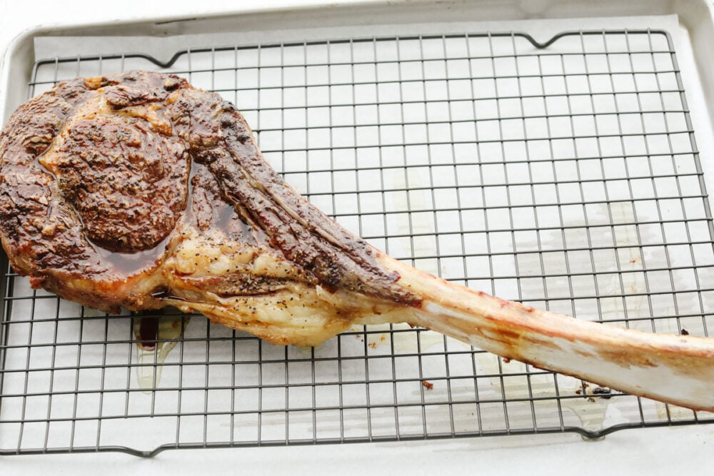 A tomahawk steak on a cooling rack, resting. 