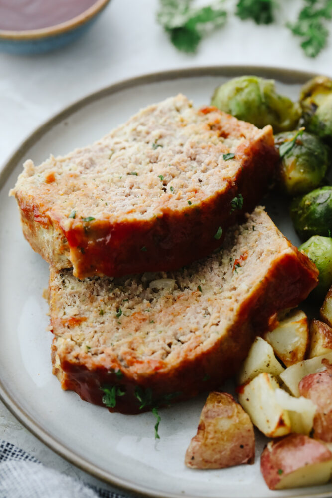 2 slices of turkey meatloaf on a plate with potatoes and brussels sprouts.
