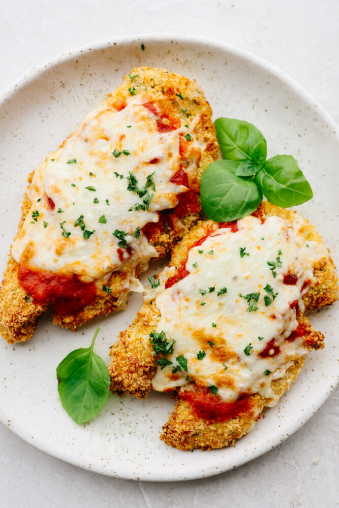 2 pieces of air fryer chicken parmesan with herb garnish on a white plate.