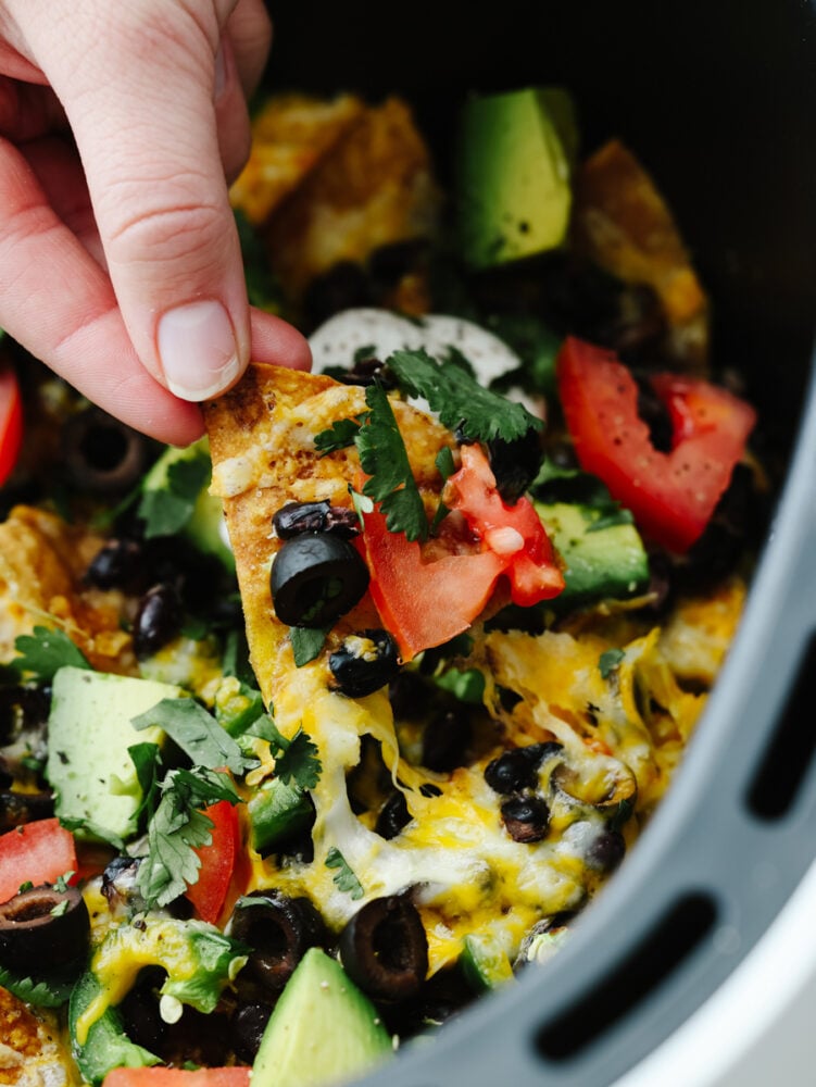 A hand scooping a nacho out of an air fryer. 