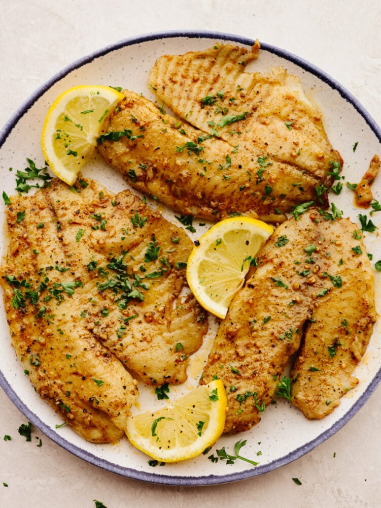 Cooked air fryer tilapia with lemon garnish on a white plate.