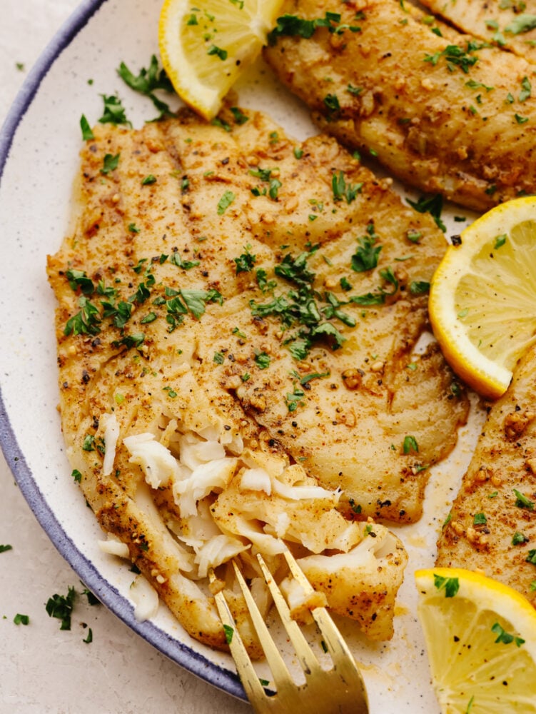 Breaking off a piece of a tilapia fillet with a fork.