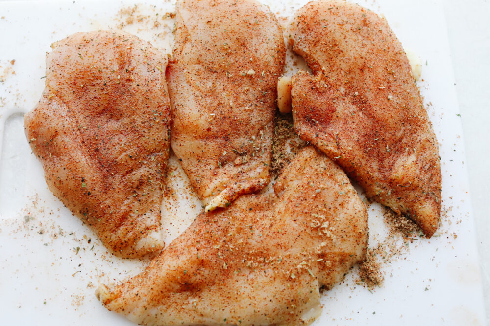 4 pieces of raw chicken breasts with seasonining rubbed on top. 