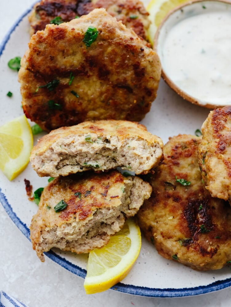 Chicken patties on a platter with tartar sauce. One of the patties is broken open. 