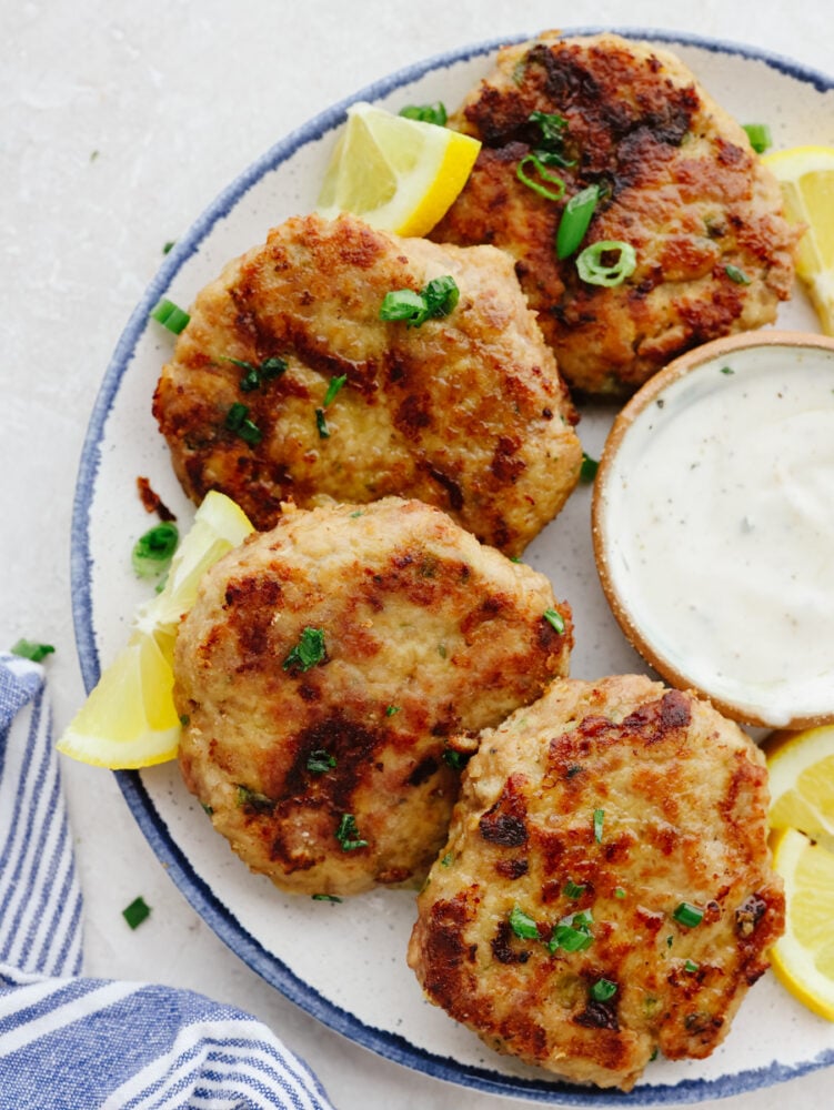 Chicken patties on a platter with some lemons and tartar sauce. 