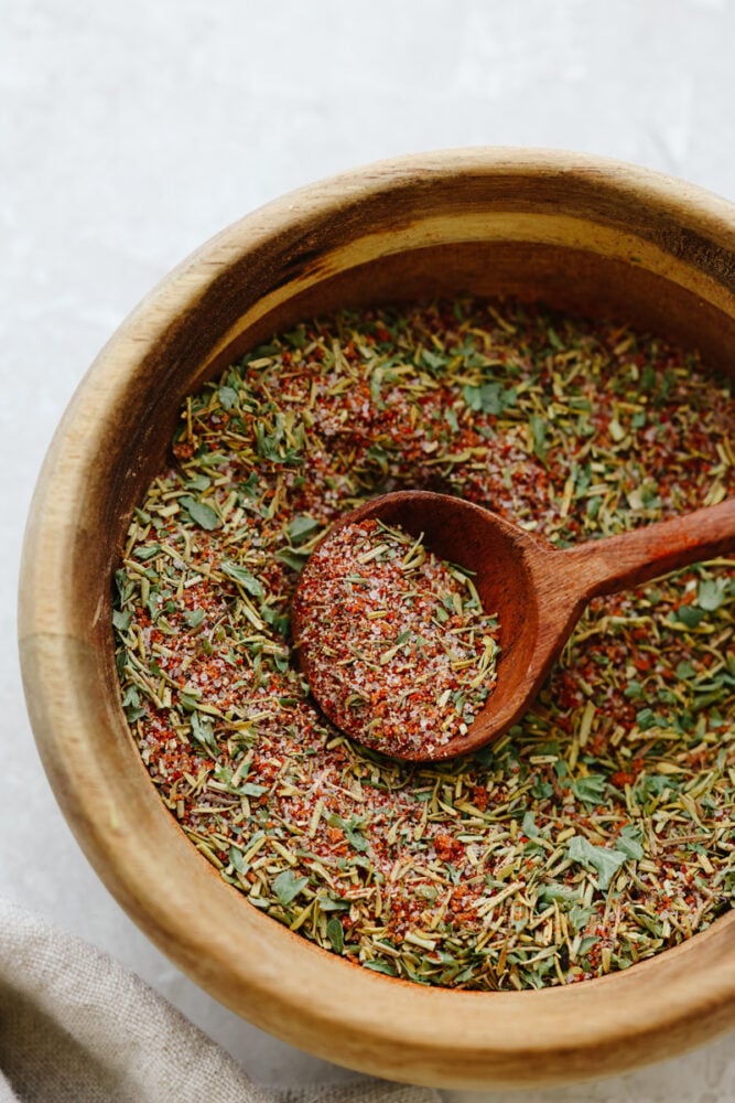 A wooden bowl with a wooden spoon filled with chicken seasoning. 