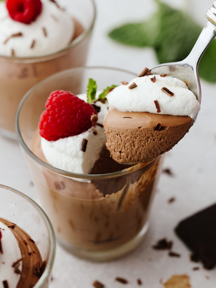 Chocolate mousse in a glass cup with a silver spoon scooping out a bite. 
