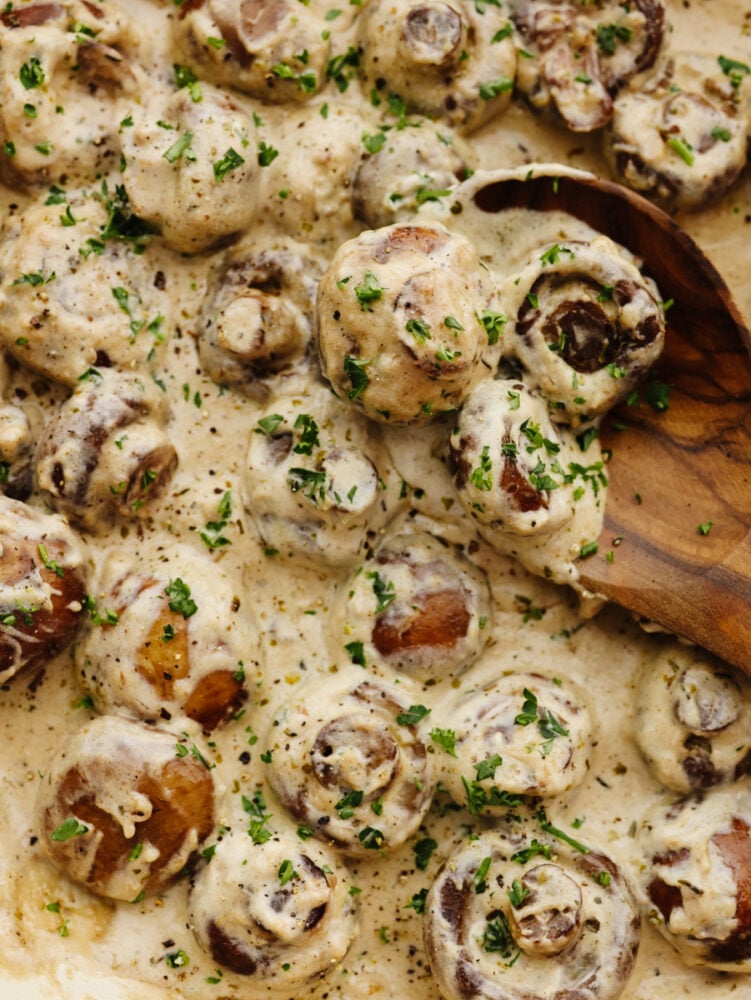 Creamy, garlic parmesan mushrooms being served with a wooden spoon. 