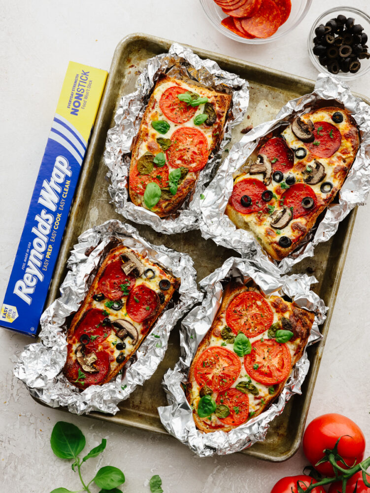 French bread pizzas wrapped in foil on a baking sheet. 