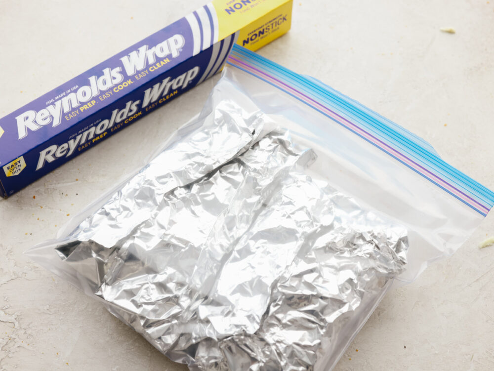 Pizza being wrapped in foil and stored in a freezer bag to store. 