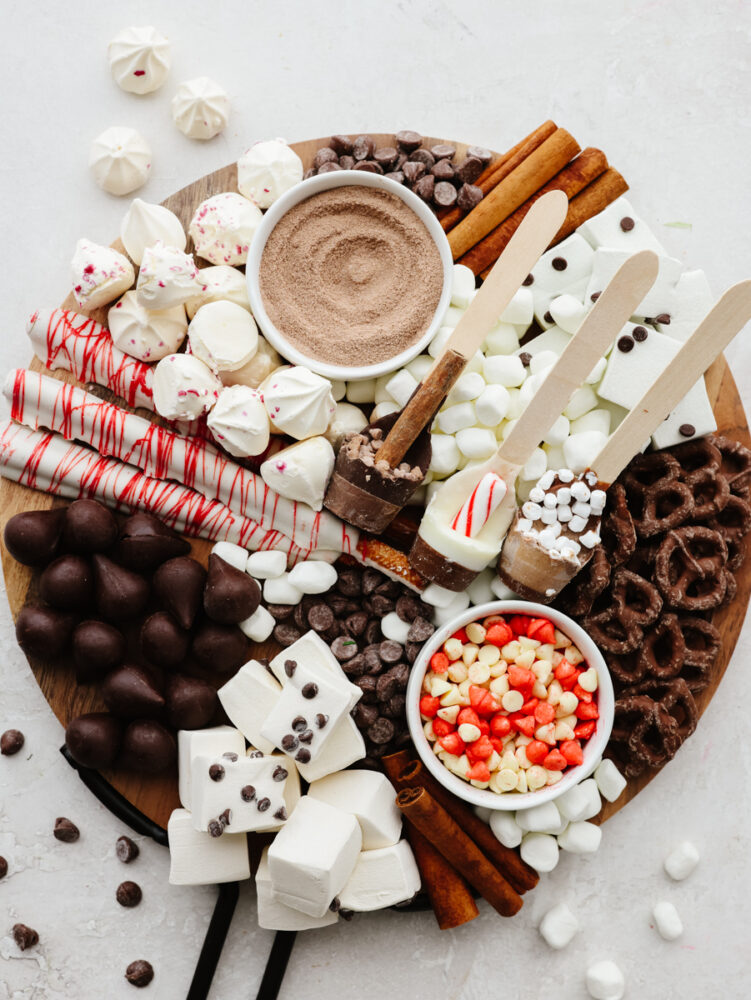 A round cutting board filled with hot chocolate toppings and mix-ins. 