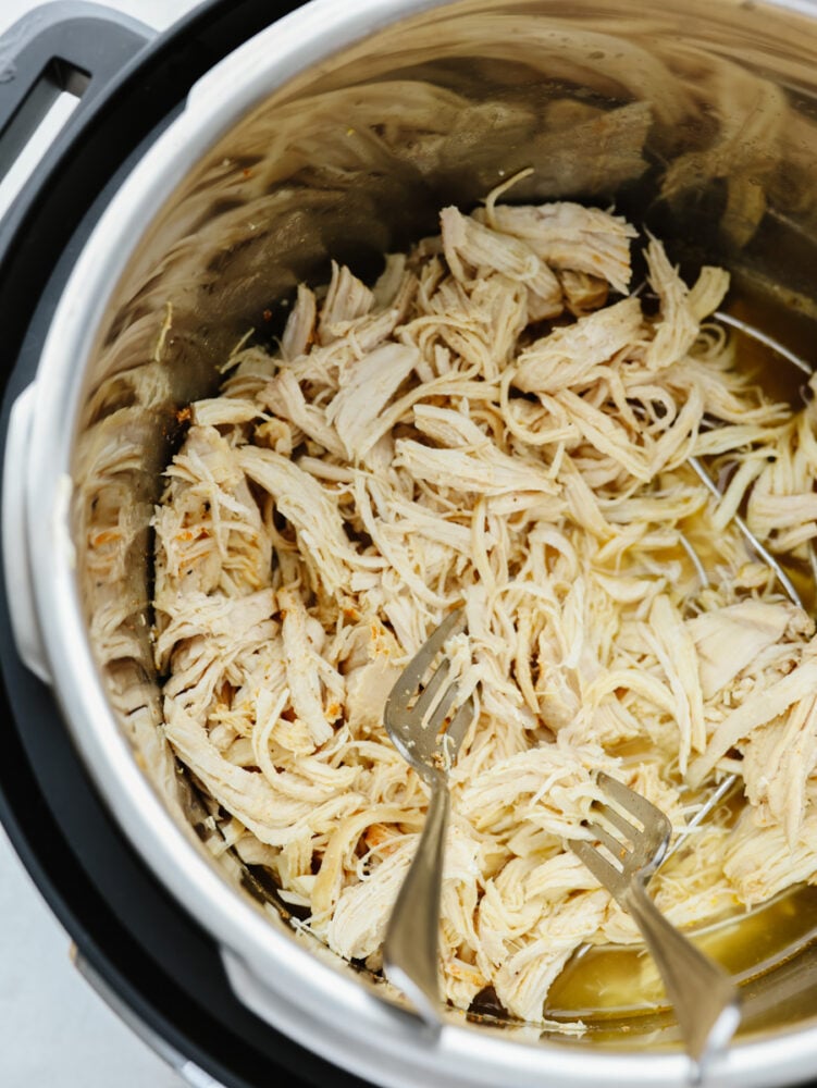 Chicken being shredded with two forks in and instant pot.