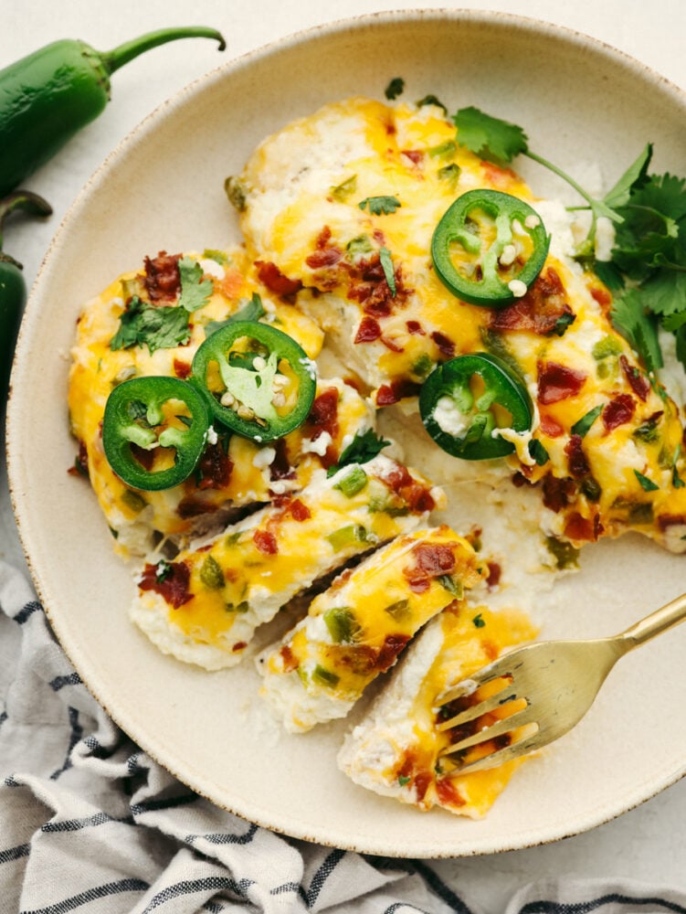 Two cooked chicken breasts topped with cheese, bacon and jalapenos, one cut into pieces.