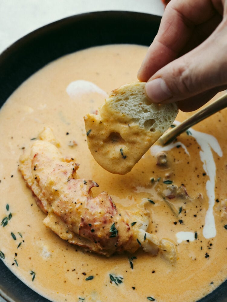 Bread being dipped into a bowl of lobster bisque. 