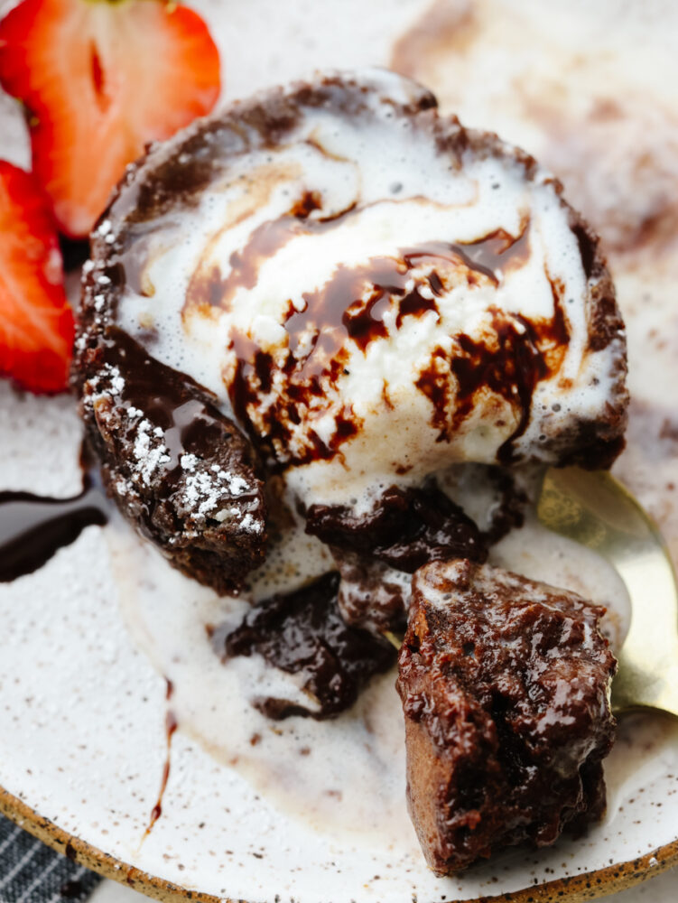 A close up of chocolate lava cake with melting ice cream and a spoon cutting into it. 