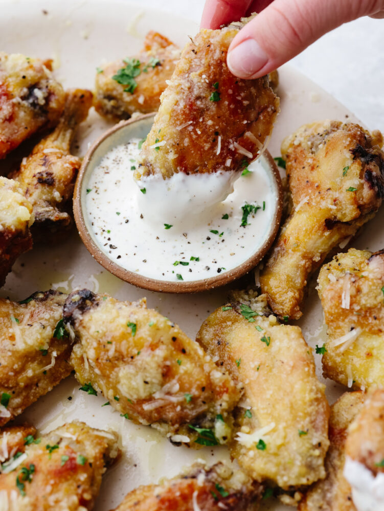 If you love wings, then these parmesan garlic ones are going to blow you away! The parmesan, honey, and garlic sauce are so delicious that these wings are going to fly off of your table! A parmesan garlic wing being dipped into ranch dressing.