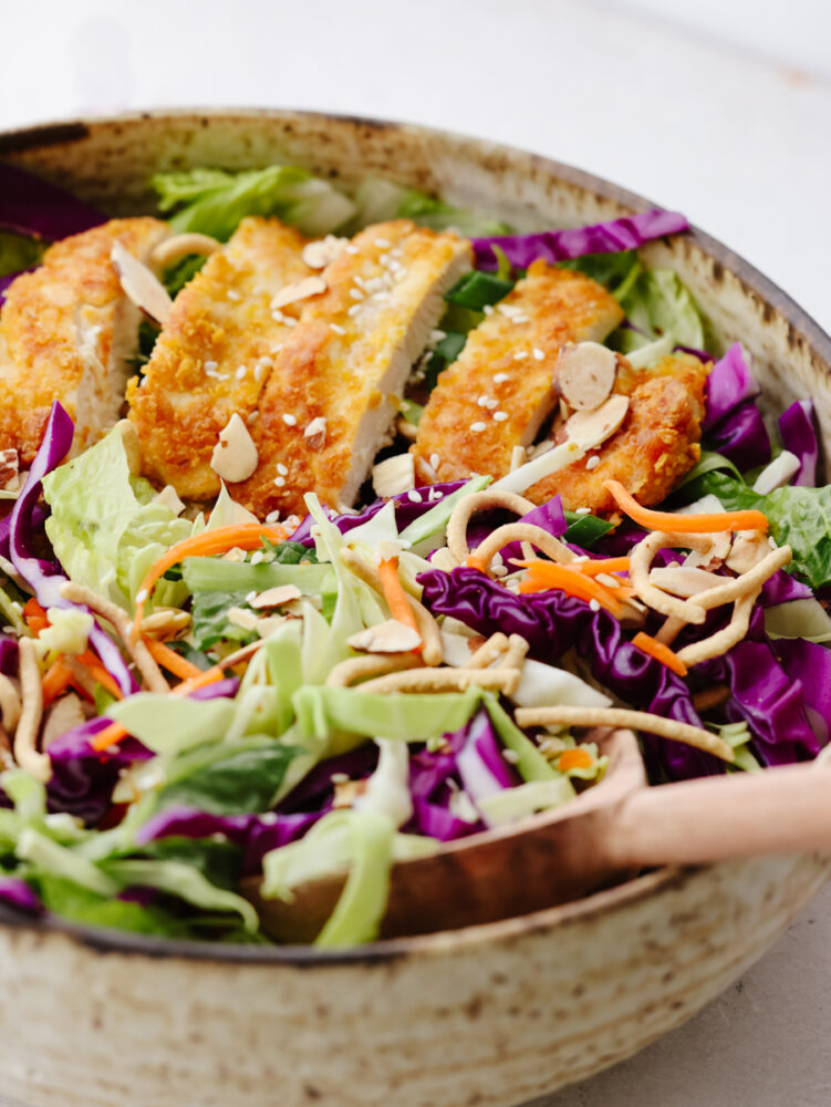 A close up of Asian chicken salad being mixed with a wooden spoon. 