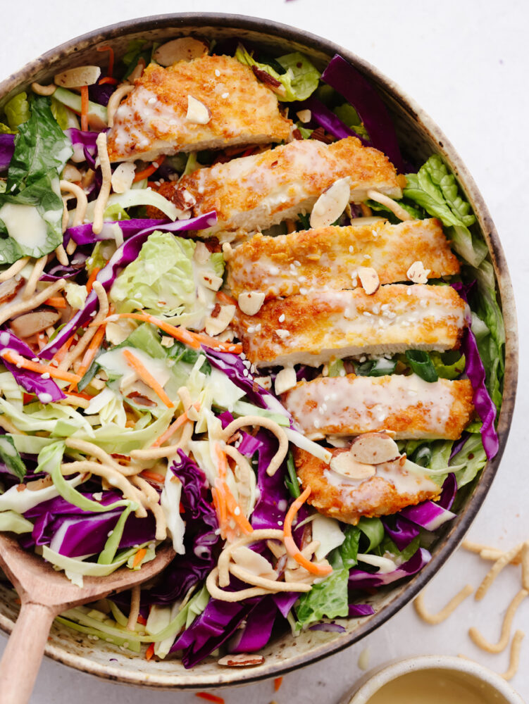 The top view of Asian chicken salad with dressing in a bowl with a wooden spoon. 