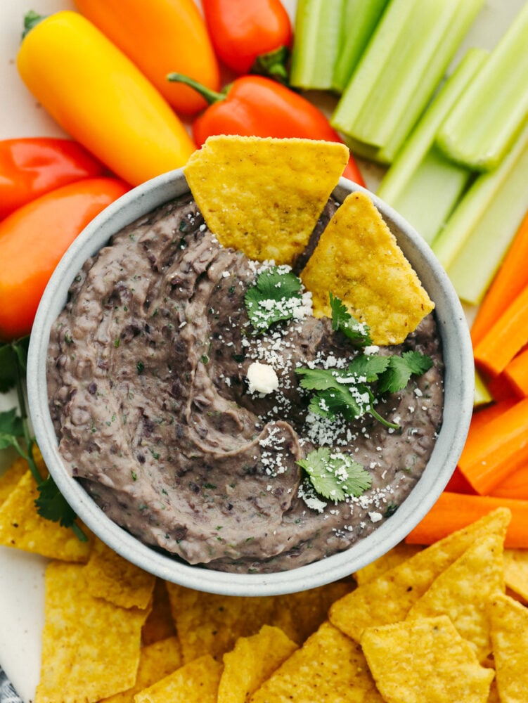 This black bean dip flavored with garlic, lime, and spices is going to be the star of your next party! It whips up in minutes and is absolutely irresistible. Closeup of black bean dip surrounded by an assortment of chips and vegetables.