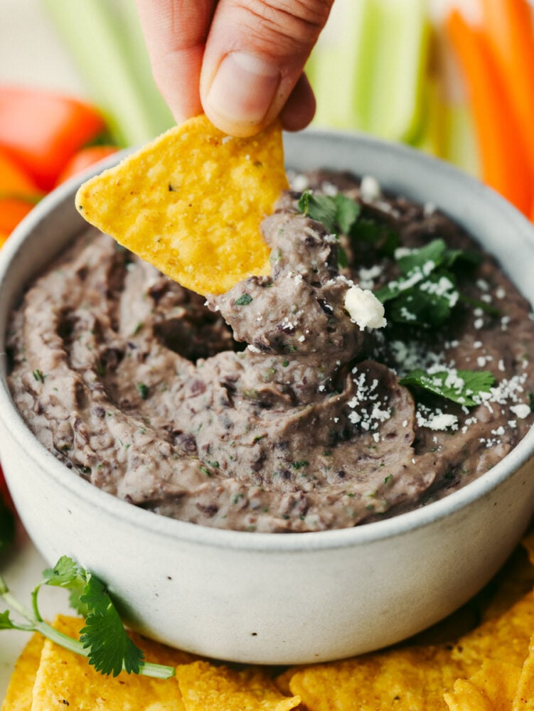 This black bean dip flavored with garlic, lime, and spices is going to be the star of your next party! It whips up in minutes and is absolutely irresistible. Dipping a chip into a bowl of bean dip.