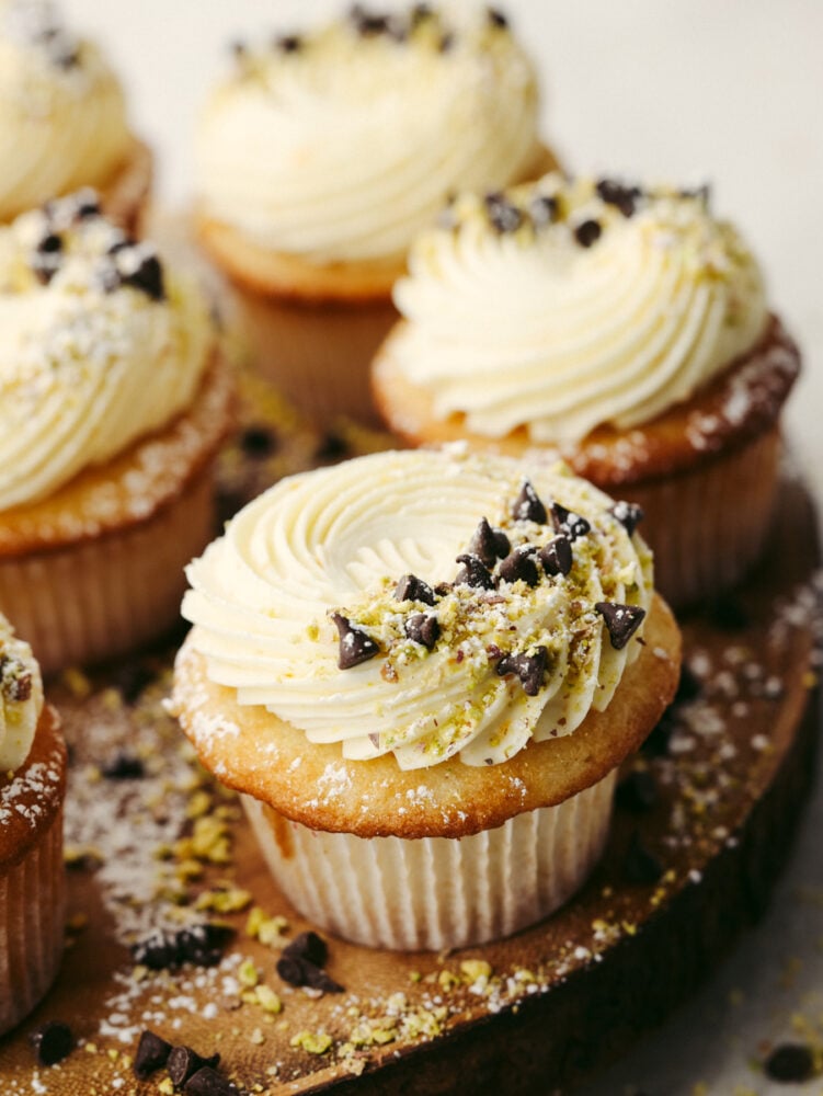 Closeup of a cupcake topped with mascarpone frosting, chocolate chips, and pistachio pieces.