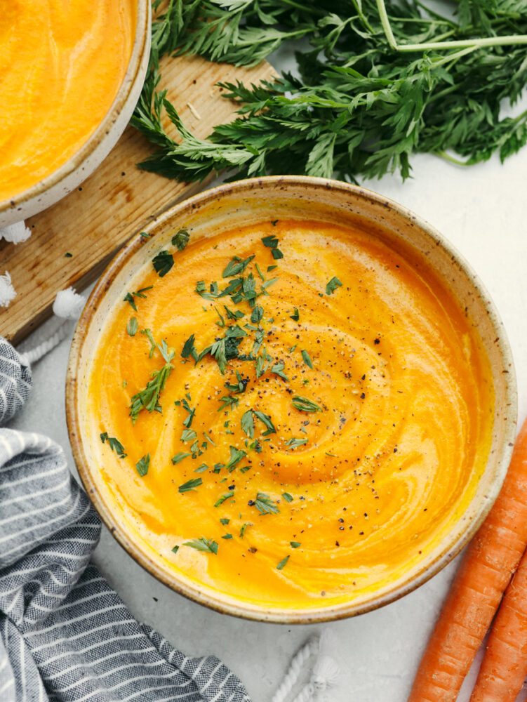 A top view of a bowl of carrot soup next to some large carrots. 
