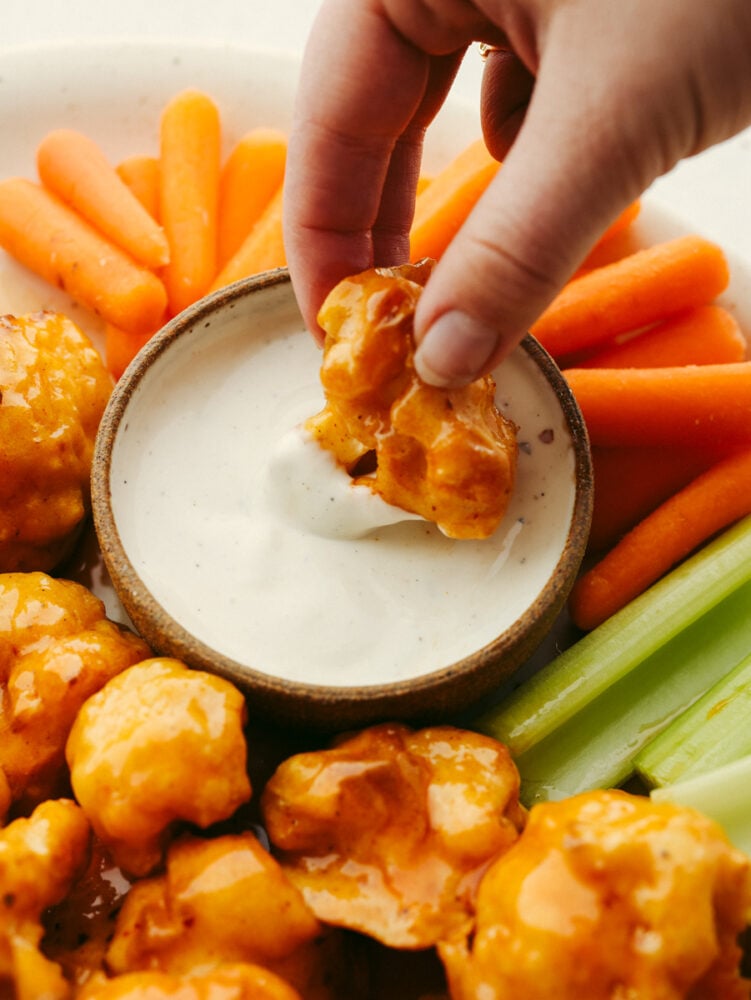 Cauliflower wings on a platter with one being dipped into ranch sauce. 
