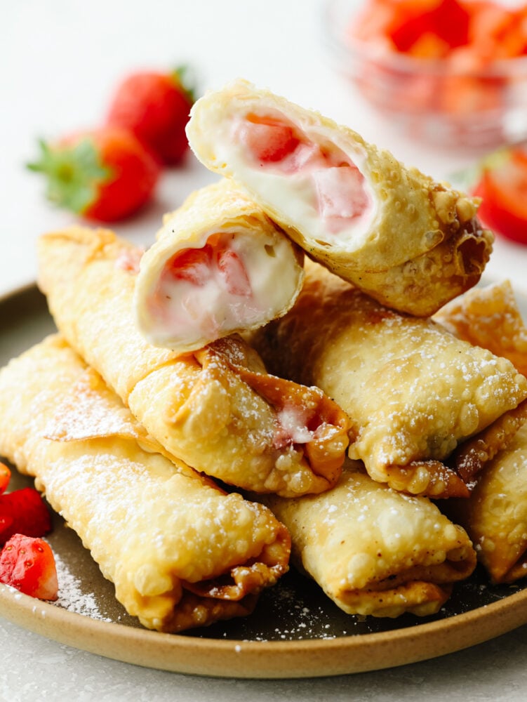 A stack of cheesecake egg rolls. The one on topis cut in half so that you can see the strawberry cheesecake filling inside. 