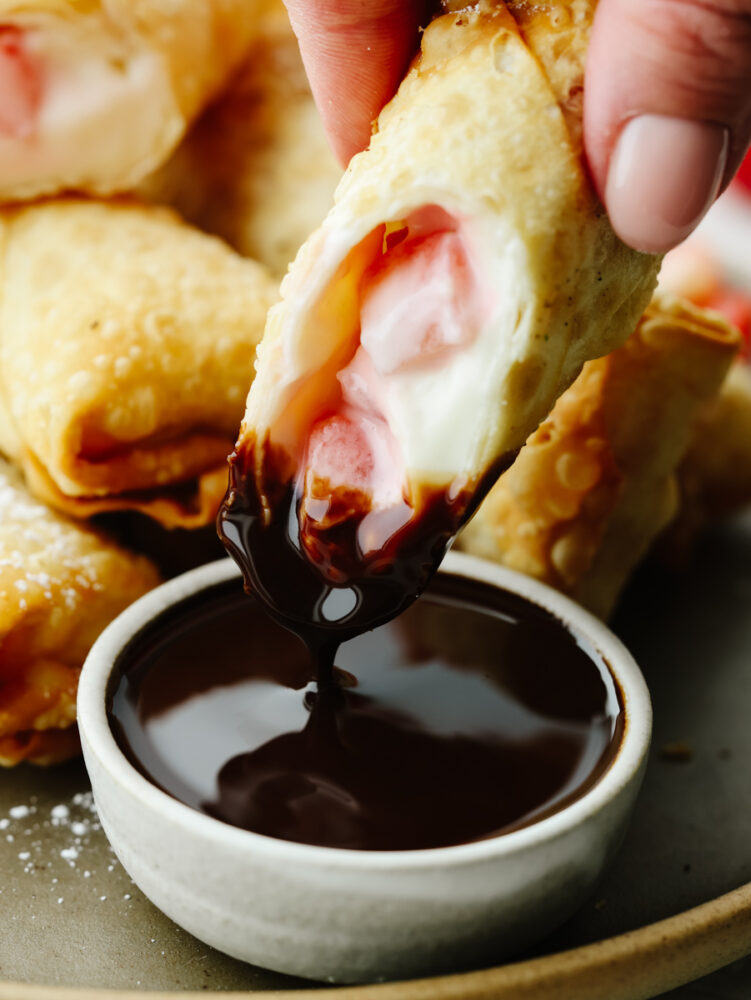 A cheesecake egg roll being dipped in chocolate sauce. 