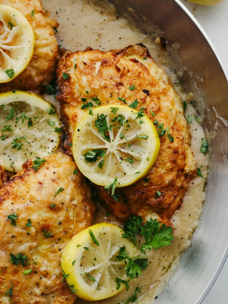 A close up of a chicken breast in a pan topped with a slice of lemon. 