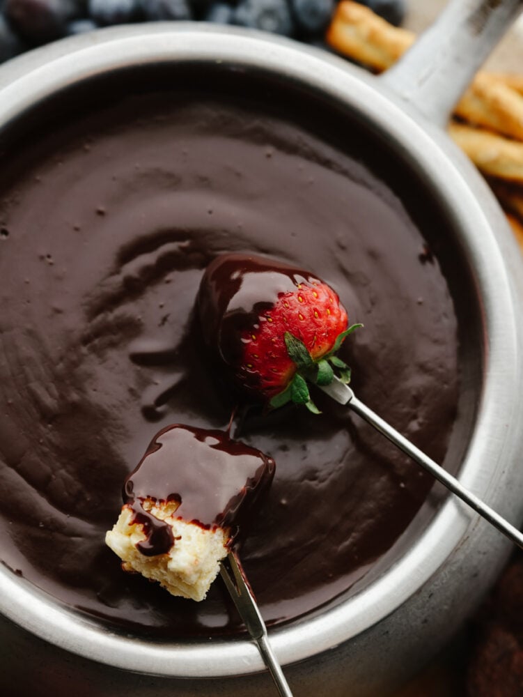 Closeup of a strawberry and marshmallow being dipped in chocolate fondue.