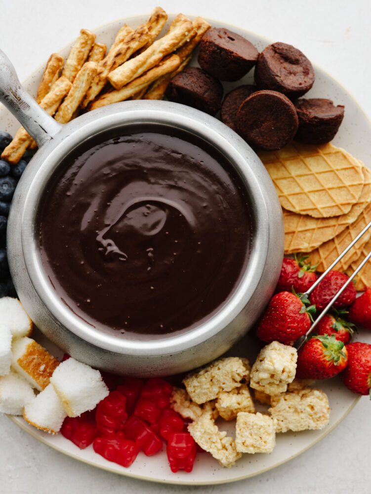 A pot of fondue surrounded by fruit, cookies, and treats.