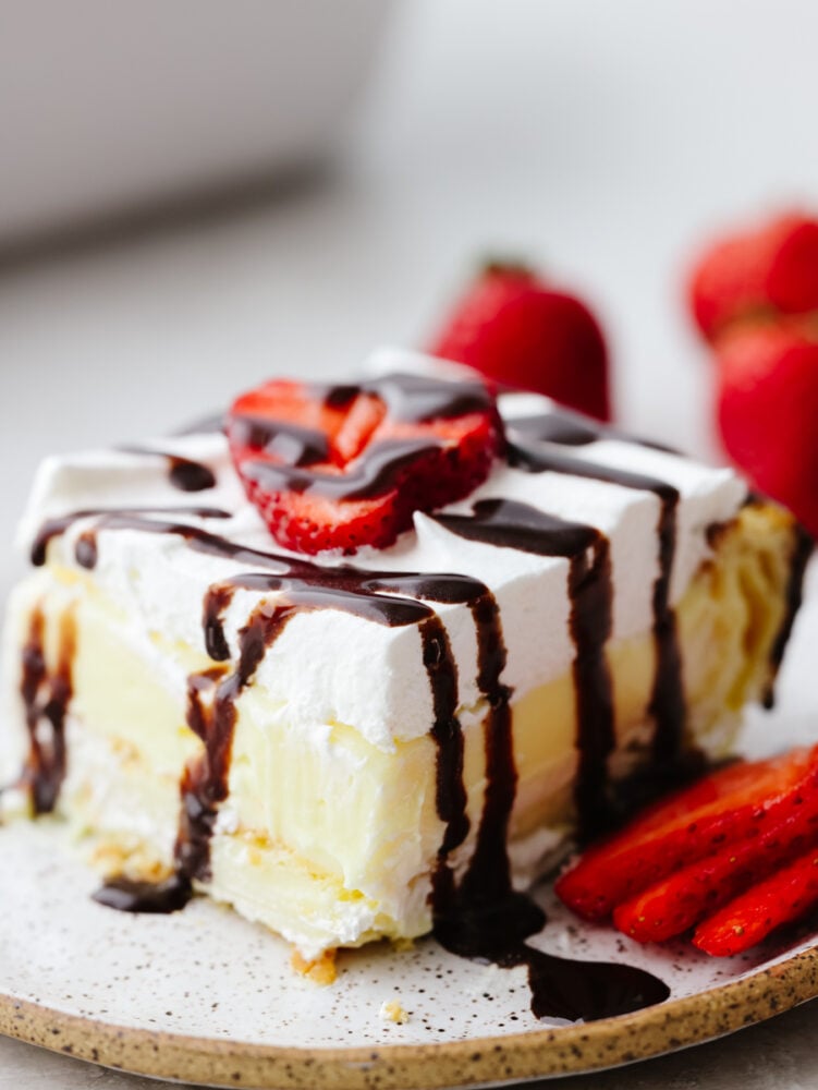 A slice of eclair cake topped with chocolate drizzle and sliced strawberries.