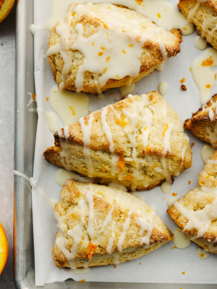 The top view of orange scones on a baking sheet topped with orange glaze. 