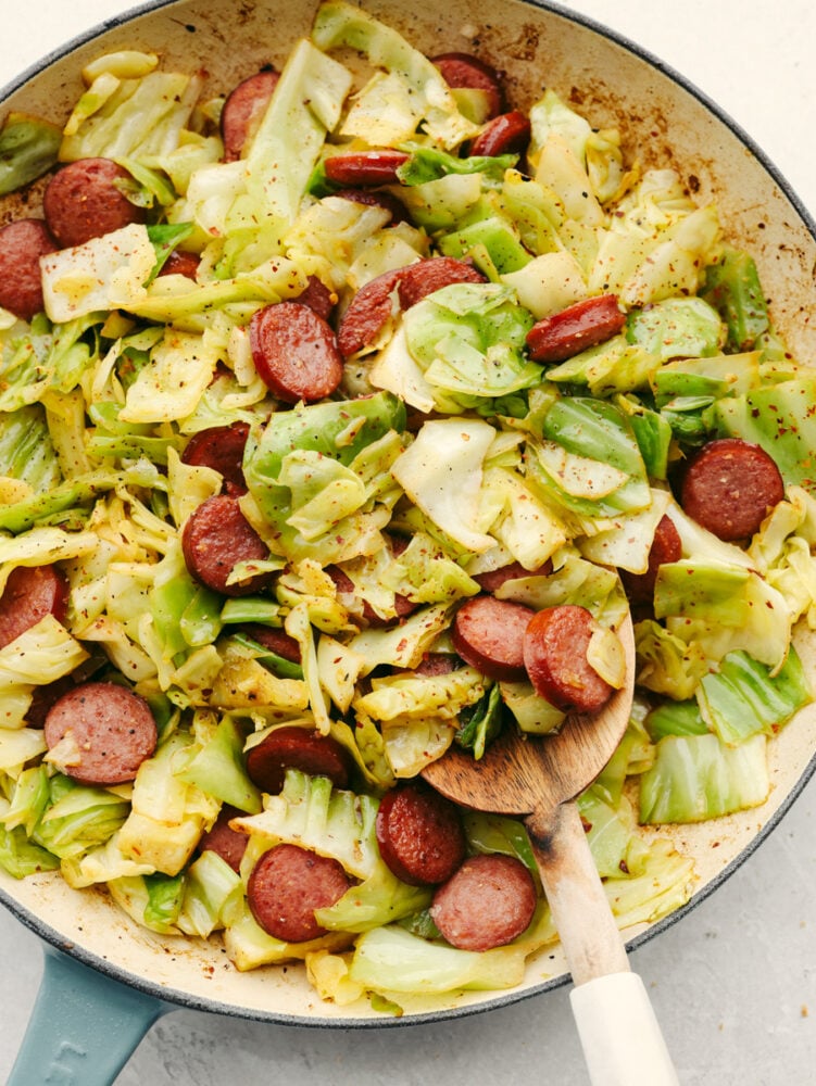 Cooked cabbage and sausage in a white skillet.