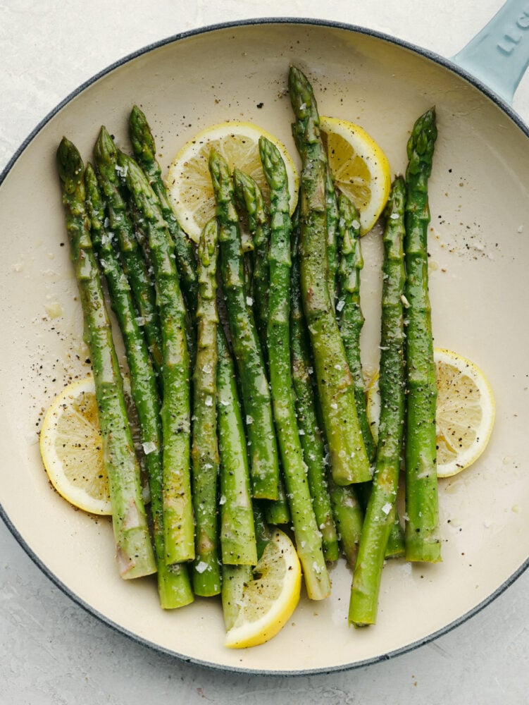 Steamed asparagus, garnished with lemon, on a white and blue plate.