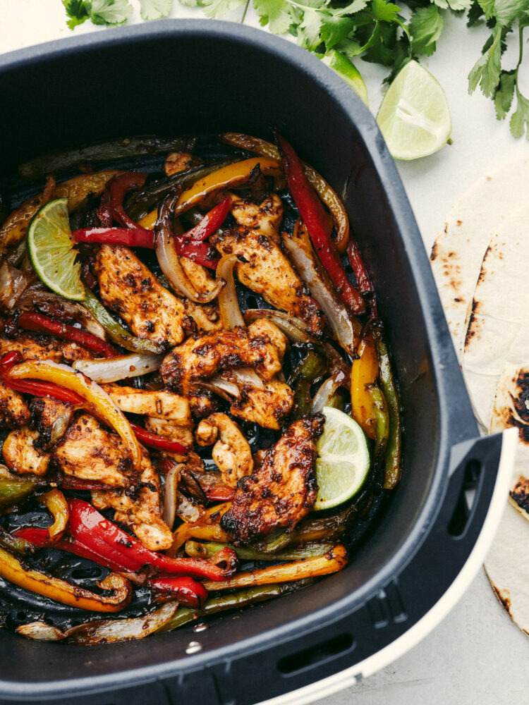 An air fryer basket filled with cooked chicken fajitas. 