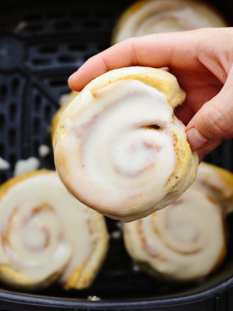 A close up of someone holding a frosted cinnamon roll. 